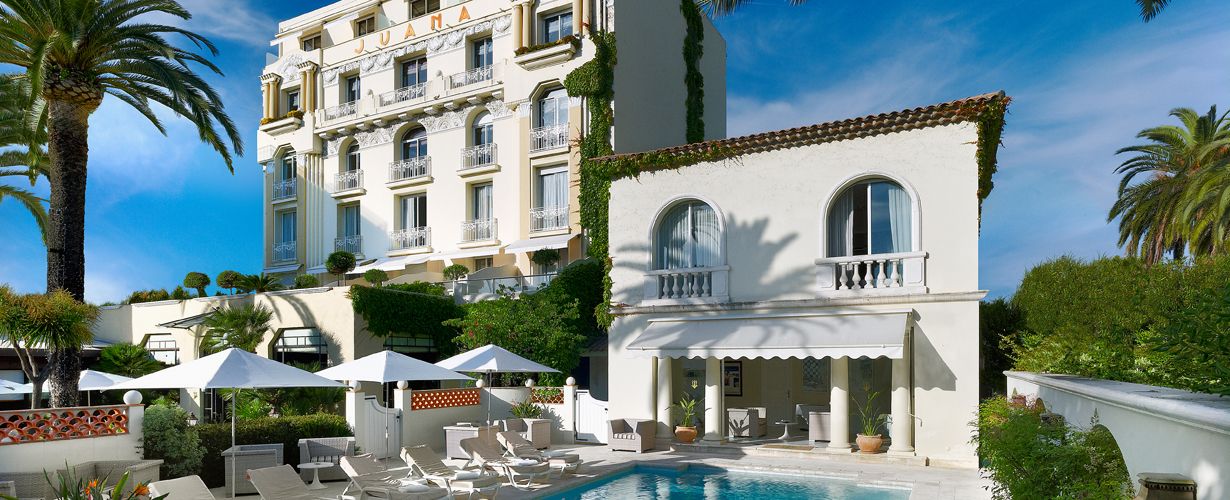 Hôtel Juana – Luxury Art Deco Hotel in Juan-les-Pins with Pool and Garden Views Elegant exterior of Hôtel Juana in Juan-les-Pins featuring palm trees, swimming pool, and sun loungers