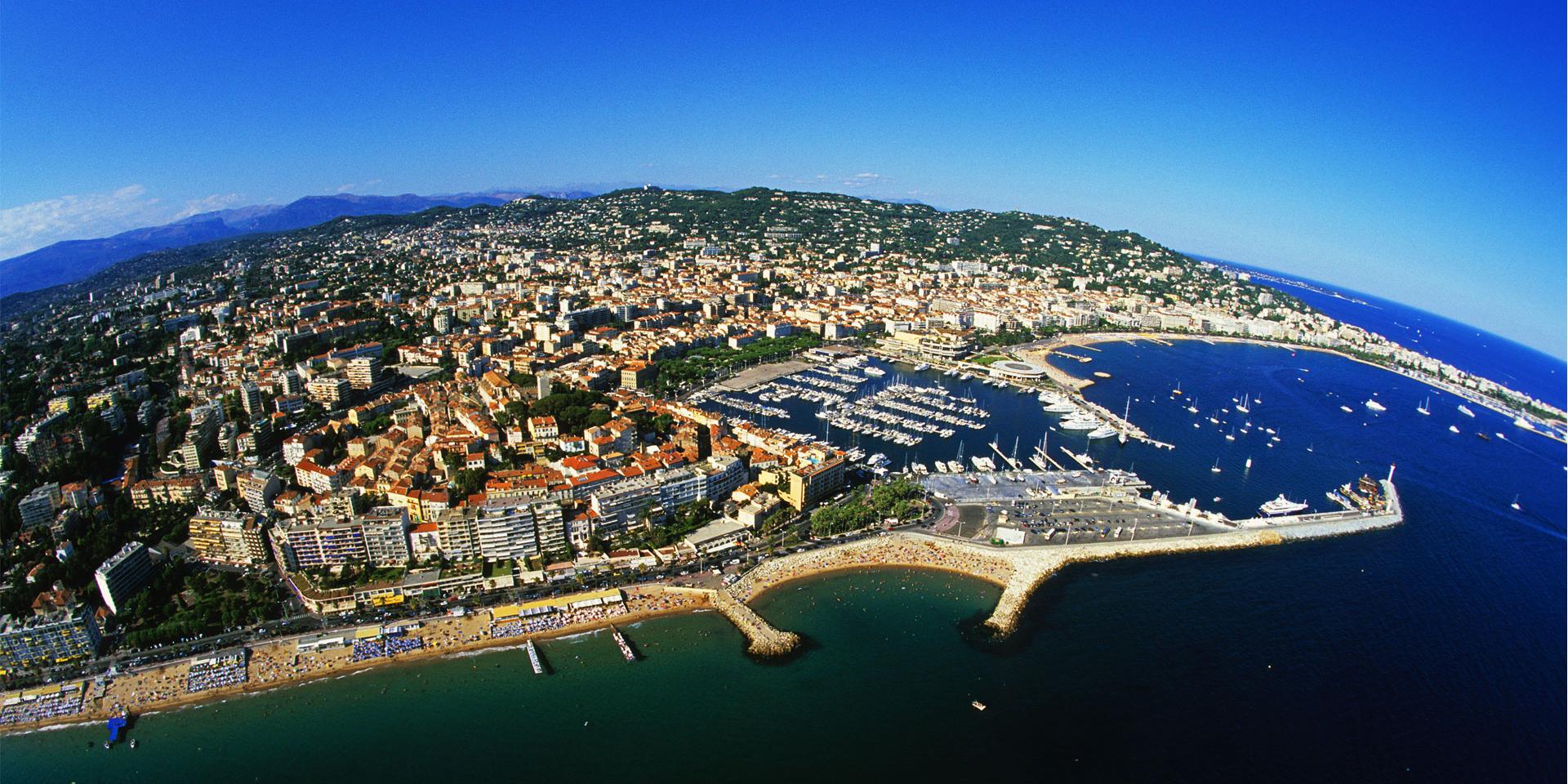 Panoramic aerial view of Cannes, its harbor and coastline under a bright blue sky