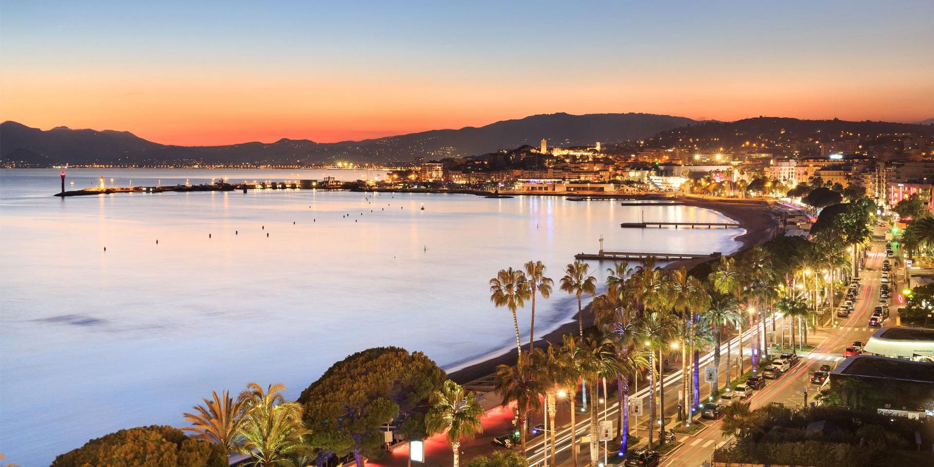 Soft orange sunset over Cannes with silhouettes of families strolling the Croisette