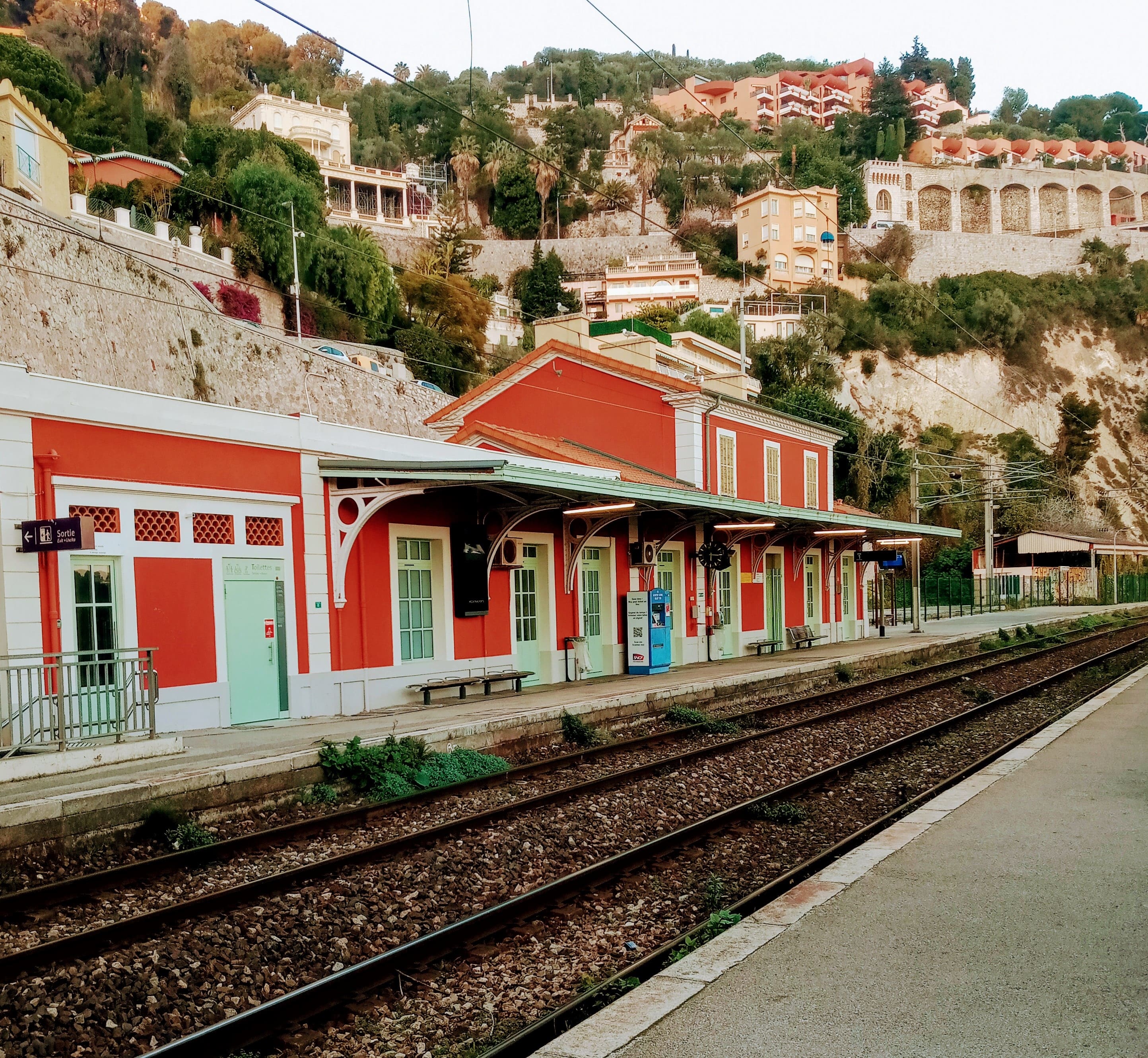 Small TER train entering Villefranche-sur-Mer station with bright blue sea beyond the platform